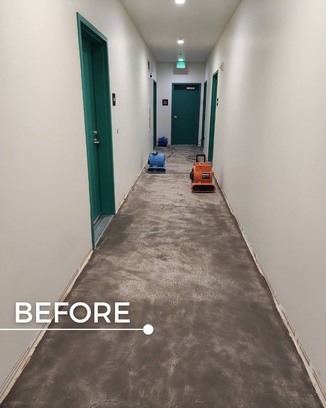Building corridor stripped to bare concrete with air movers running after water damage