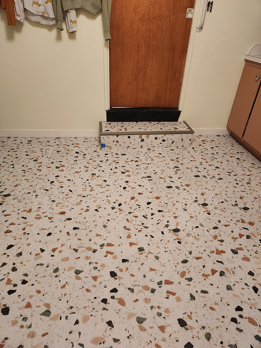 Terrazzo-look vinyl flooring at a room entry, finished to the baseboard